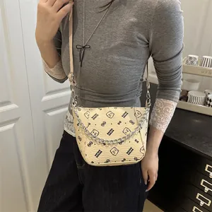 Sac seau beige chic avec motifs ours, chaîne métal et bandoulière porté par un mannequin