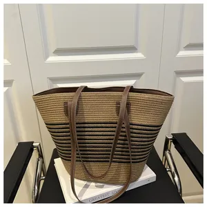 Detail of straw woven tote with black stripes and brown faux leather handle stitching