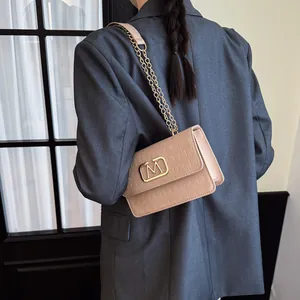 Bolso bandolera rosa con textura de cocodrilo y cierre metálico dorado en forma de M