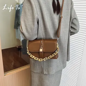 Classic brown PU leather crossbody bag with bold gold chain and padlock detail on gray suit