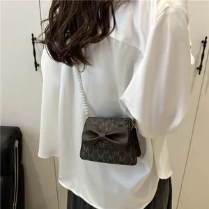 Girl's brown bow handbag with M-pattern and pearl chain strap on a white shirt