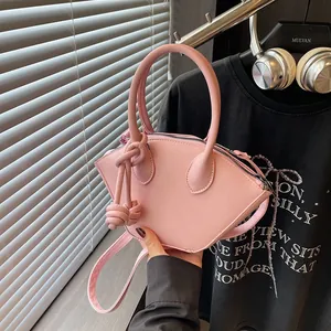 Pink minimalist shell-shaped handbag with knot charm and crossbody strap in a modern setting
