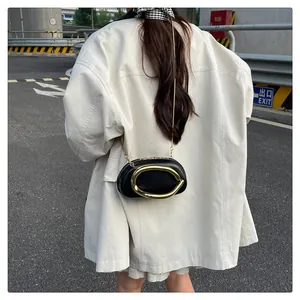 Détail d'un sac bandoulière chic en cuir noir avec boucle dorée et chaîne sur une tenue