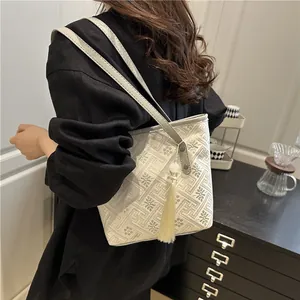 Elegant beige tote bag with retro geometric weave and tassel detail shown on shoulder