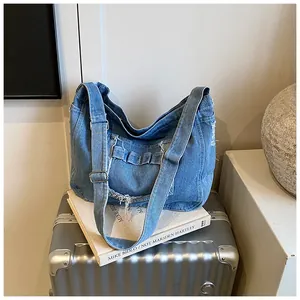 Detail of blue denim hobo bag with frayed edges and silver metal buckle on books