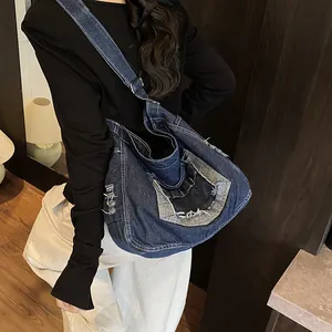 Large distressed blue denim crossbody bag with vintage frayed edges shown on a model