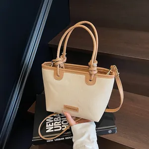 Large straw tote bag with brown leather trim and handles on wooden stairs