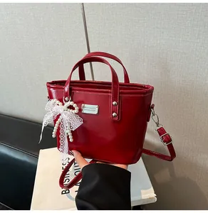 Close-up of a burgundy patent leather bucket bag with pearls and a lace bow detail