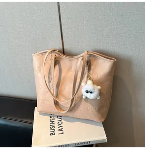 Close-up of beige faux leather tote bag with embossed flowers and plush ball pendant
