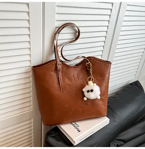 Detail view of brown embossed tote bag featuring dual handles and a fuzzy monster charm