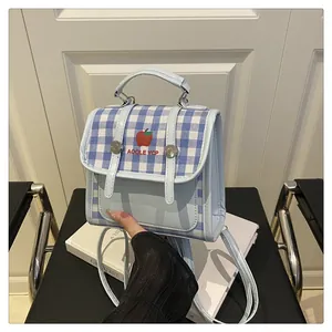 Detail of light blue mini backpack with blue plaid flap and embroidered apple motif