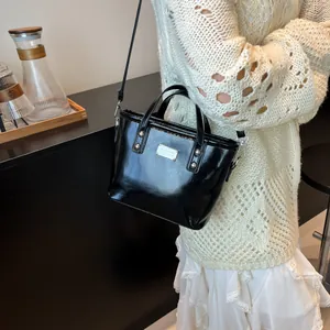 Elegant black patent leather bucket bag with top handle and metallic logo plaque