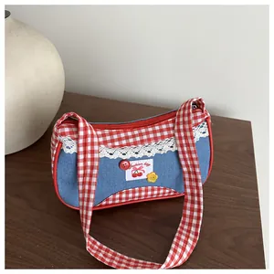 Detail of blue denim bag with gingham handles, lace trim, and cherry patch