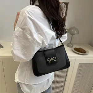 Minimalist black saddle bag with golden bow buckle and shoulder strap worn by a model