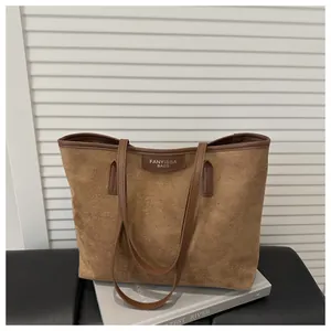 Close-up of brown suede tote bag featuring leather branding label and reinforced handles
