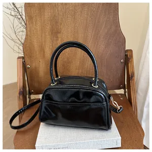 Detailed close-up of glossy black pillow bag with golden hardware on a wooden chair