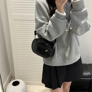 Glossy black oval crossbody bag with gold hardware and reflective PU leather finish
