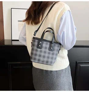 Model showing gray checkered bucket bag with leather handle and silver rivet details