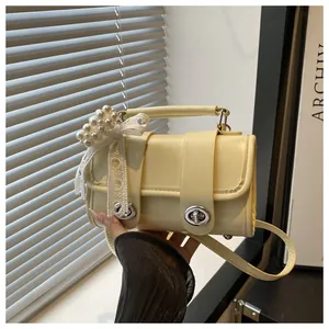 Detalle de bolso de cuero amarillo crema con colgante de perlas y lazo de encaje