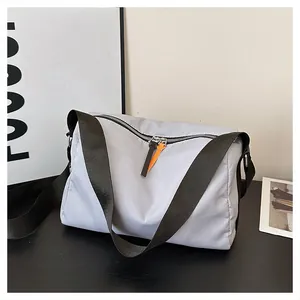 Detailed view of light gray nylon crossbody bag with dual-color zipper pulls on black desk