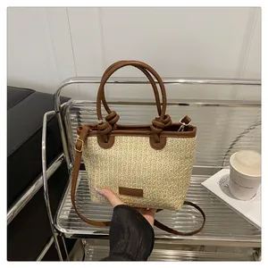 Detailed view of woven straw bag with brown leather handles and decorative knots