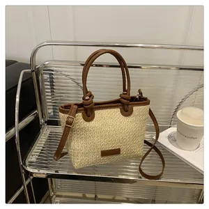 Detail of woven straw tote bag featuring brown leather handles and knot design