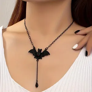 Close-up of gothic black bat necklace featuring a ruby heart and drop tassel on model