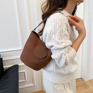 Sac seau rétro minimaliste en daim marron porté avec un pull en tricot blanc sur fond blanc