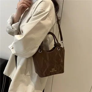 Brown pleated bucket bag with dual handles and crossbody strap on white coat model