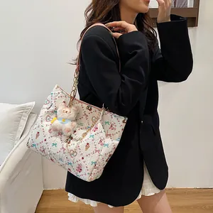 Elegant cream patterned tote bag with bear charm and pearl chain accessory on model