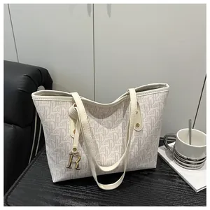 Close-up of beige tote bag with letter print and golden R-shaped metal charm