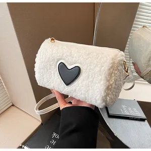 Detail of white plush cylinder bag with black heart patch and gold metal zipper closure