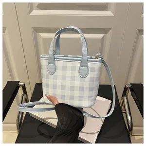 Detail of light blue gingham handbag with leather handles and adjustable shoulder strap