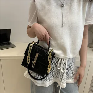 Elegant black minimalist shoulder bag with gold chain strap and top handle in a lifestyle setting
