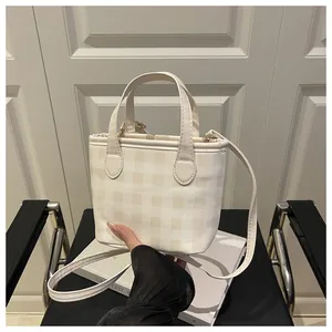 Detail of a beige checkered tote bag with top handle and slim crossbody strap