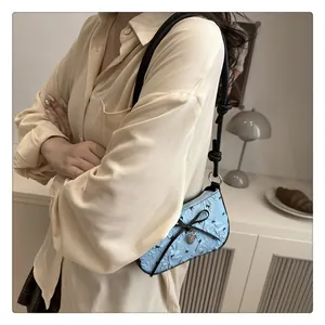 Dettaglio borsa a sella azzurra con trama a fiocco nero e ciondolo a cuore su modella