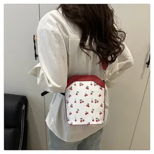 Detail view of white cherry print bucket bag with red strap and gold hardware on a model