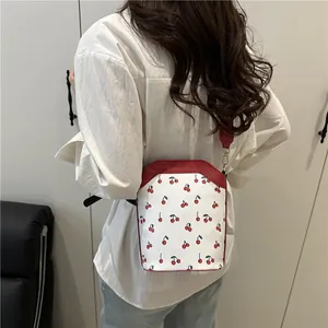 White bucket bag with red cherry prints and contrasting strap shown on a model