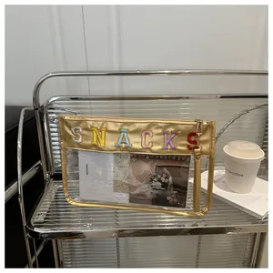 Detail of transparent PVC makeup bag with gold SNACKS letter embroidery and wrist strap