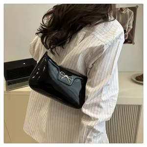 Detail of black patent leather underarm bag featuring a delicate gold metal bow accent