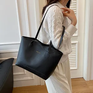 Sac fourre-tout noir en similicuir avec texte doré porté par un mannequin en pull blanc