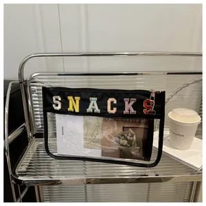 Detail of transparent PVC organizer bag featuring colorful SNACKS embroidery and zipper
