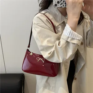 Chic burgundy patent leather shoulder bag with a gold bow accent and metallic charms