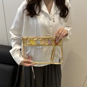 Transparent PVC cosmetic bag with gold trim and rainbow SNACK embroidery held by model