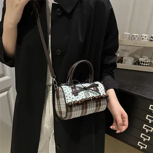 Sac polochon à pois avec nœud et breloque cœur porté sur un long manteau noir