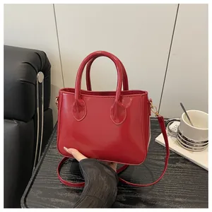 Glossy red faux leather handbag with gold metal hooks on a black wooden table