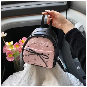 Detail of mini backpack featuring pink pleated fabric with black bow patterns and 3D bow