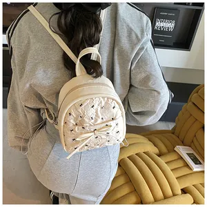 Close-up of a mini cream backpack with 3D bow details and embroidery on a female model