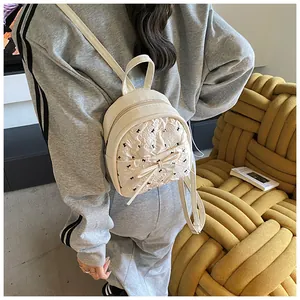 Mini cream backpack with pleated texture and black bow detail on a yellow sofa