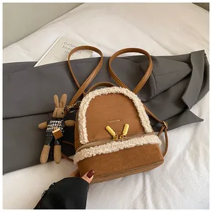 Brauner Wildleder-Rucksack mit weißem Kunstfellbesatz und Hasenanhänger auf weißem Bett